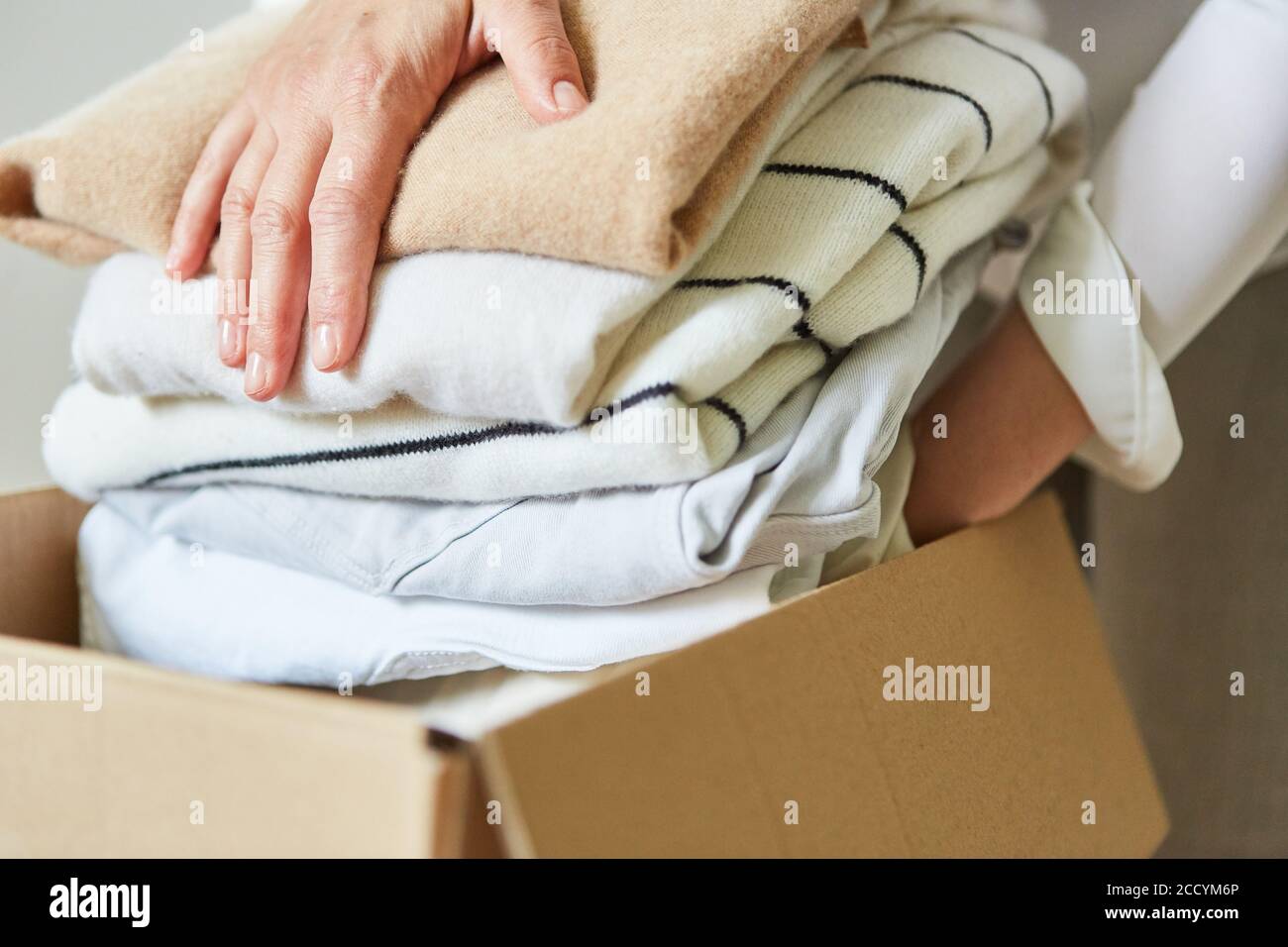 Une femme met ses vêtements dans une boîte de déménagement pour un vêtement don ou déménagement Banque D'Images