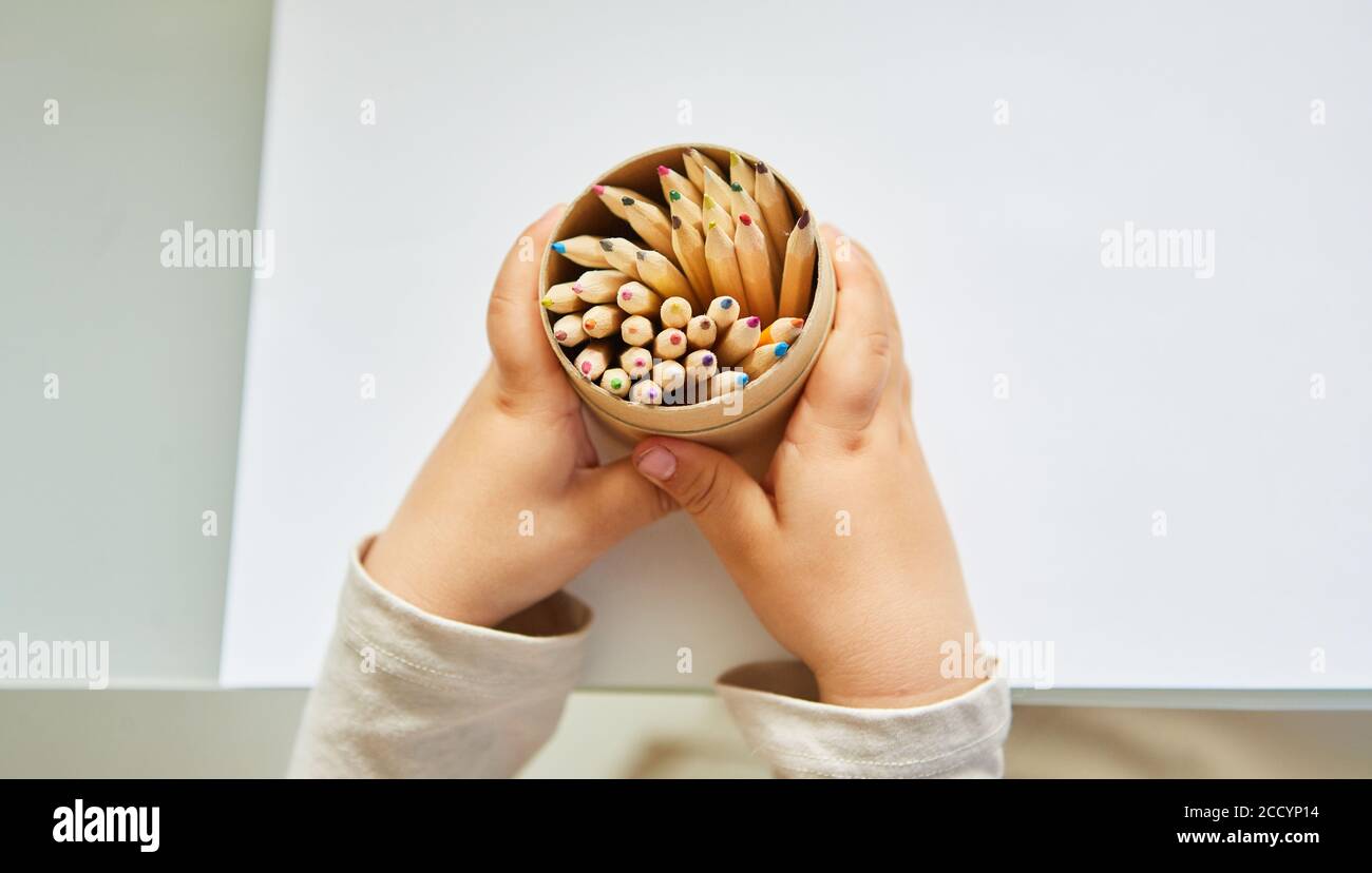 Bébé tient une tasse avec beaucoup de crayons de couleur pour dessiner dans les deux mains Banque D'Images