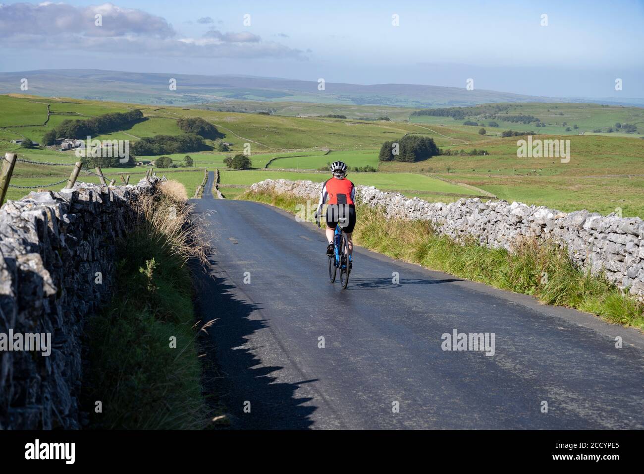 Cycliste en descendant une longue route droite vers Settle, parc national de Yorkshire Dales, Royaume-Uni. Banque D'Images