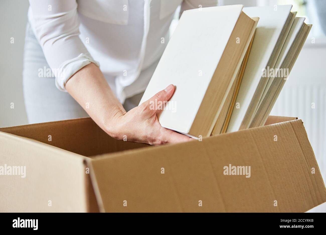 Une femme décompresse des livres d'une boîte mobile lorsqu'elle les déplace vers un nouvel appartement Banque D'Images