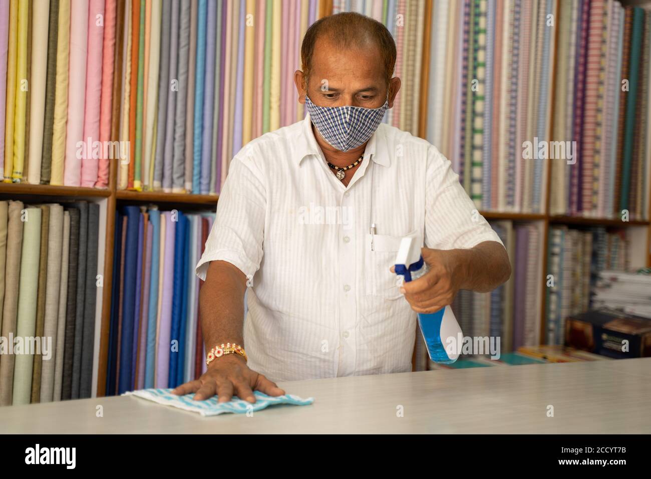 Le commerçant dans la table de désinfection du masque médical en utilisant de l'assainisseur - nettoyer la poussière sur la surface du bureau avec un chiffon ou un désinfectant en aérosol, à protéger de Banque D'Images