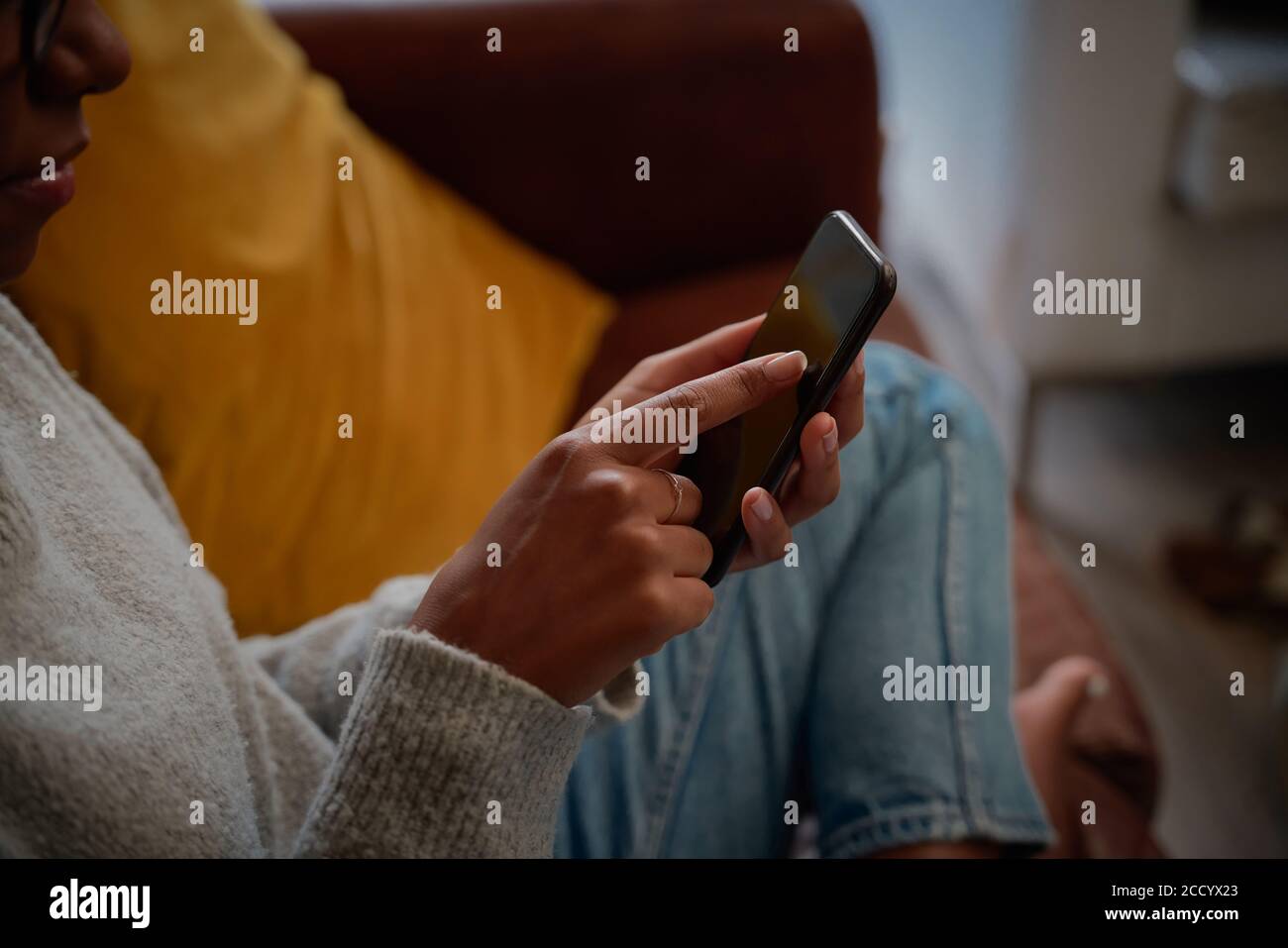 Gros plan de la main de la jeune femme touchant l'écran du téléphone portable assis sur un canapé Banque D'Images