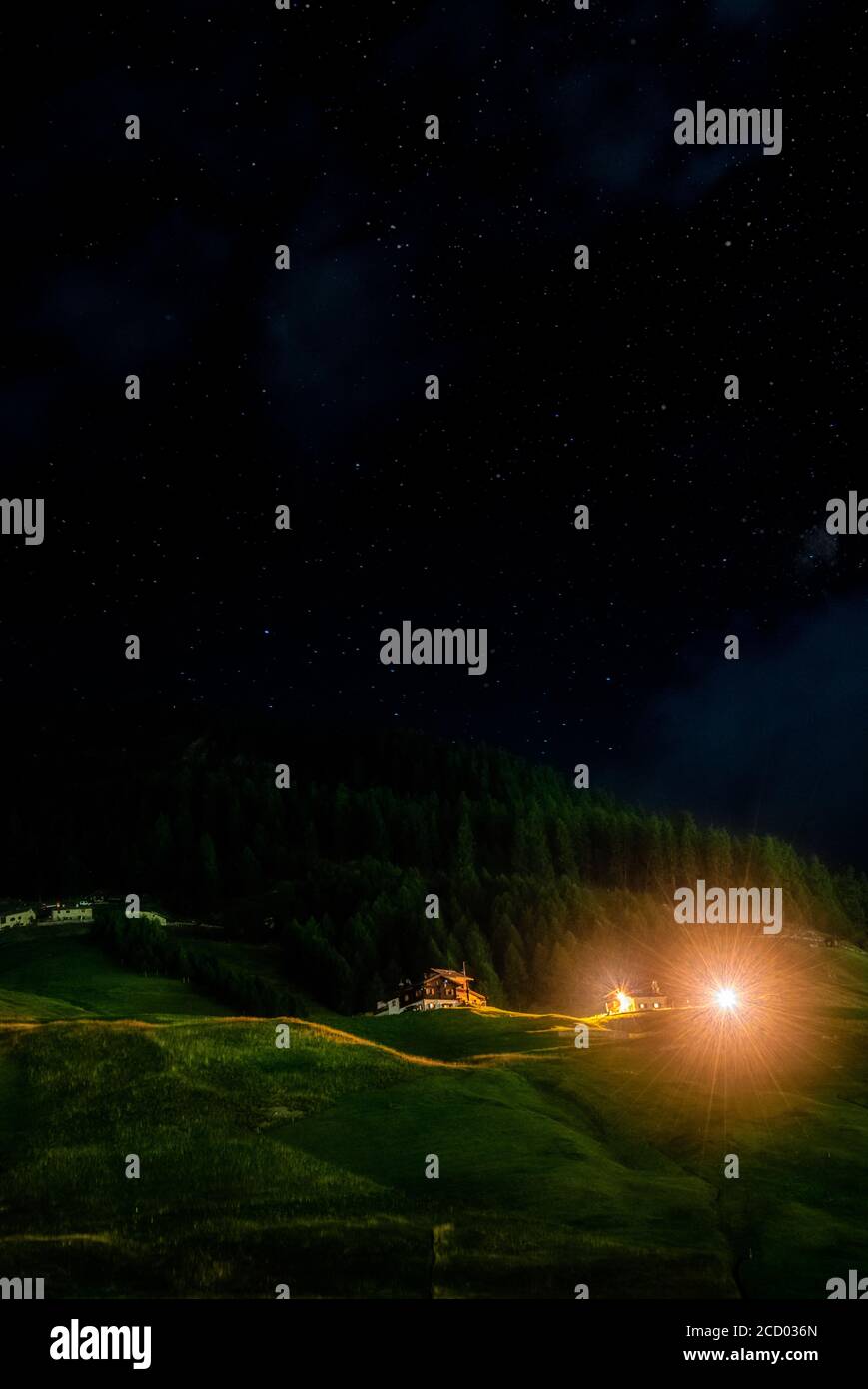 Scène rurale de nuit alpine en Italie, Europe avec chalet lumineux sur une pente verdoyante de montagne verte avec des arbres forestiers donnant sur la vallée de verti Banque D'Images