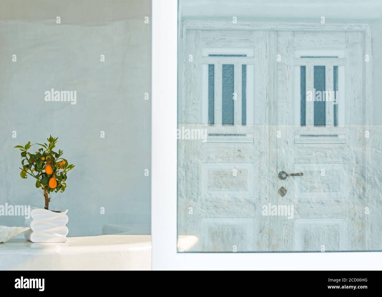 Atmosphère cycladique dans la ville d'Oia, sur l'île de Santorin, avec un bonsaï et une porte blanche reflétée dans un miroir le long du trajet Banque D'Images