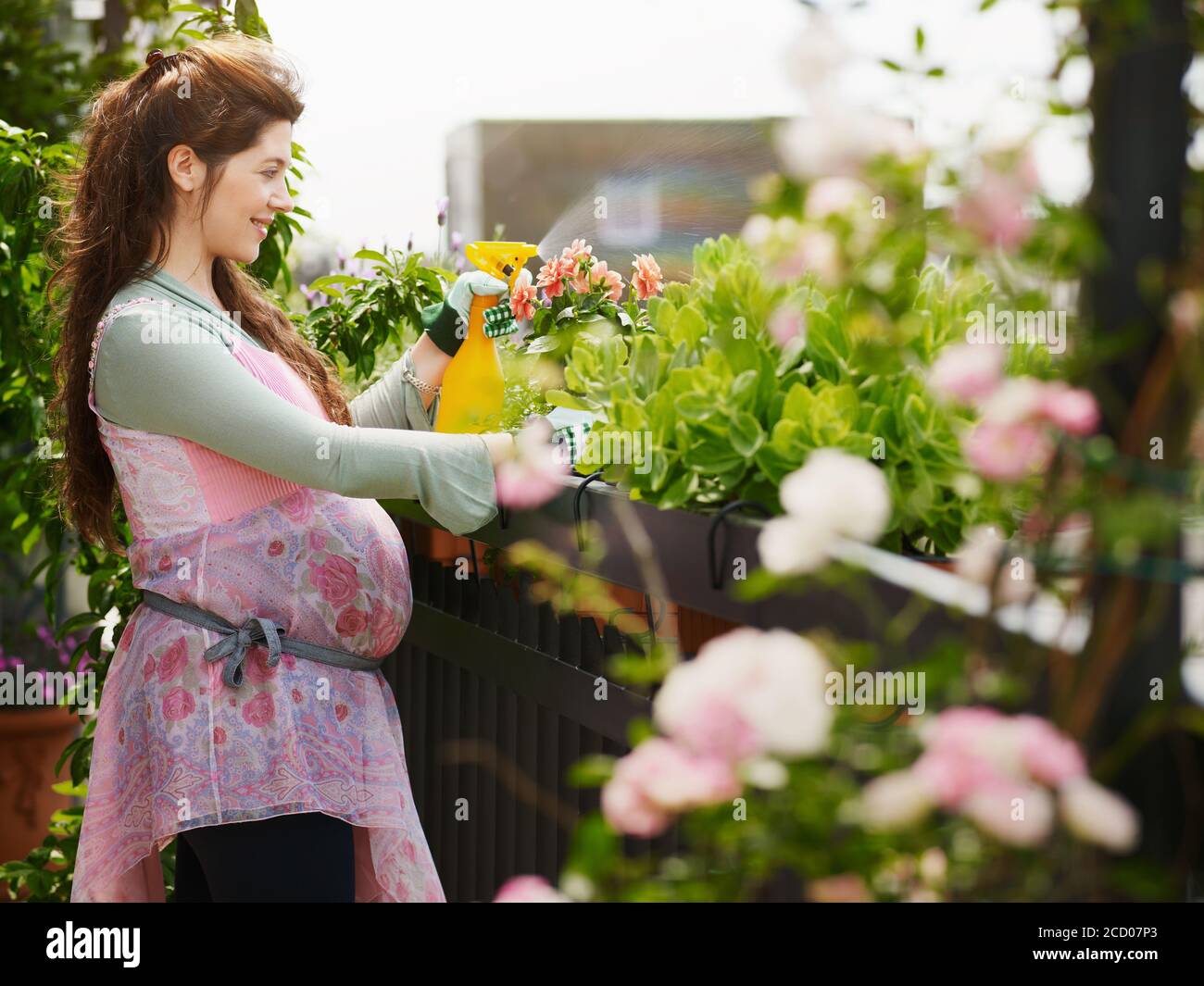 Jeune femme enceinte pulvérisant de l'eau sur des plantes et des fleurs Banque D'Images