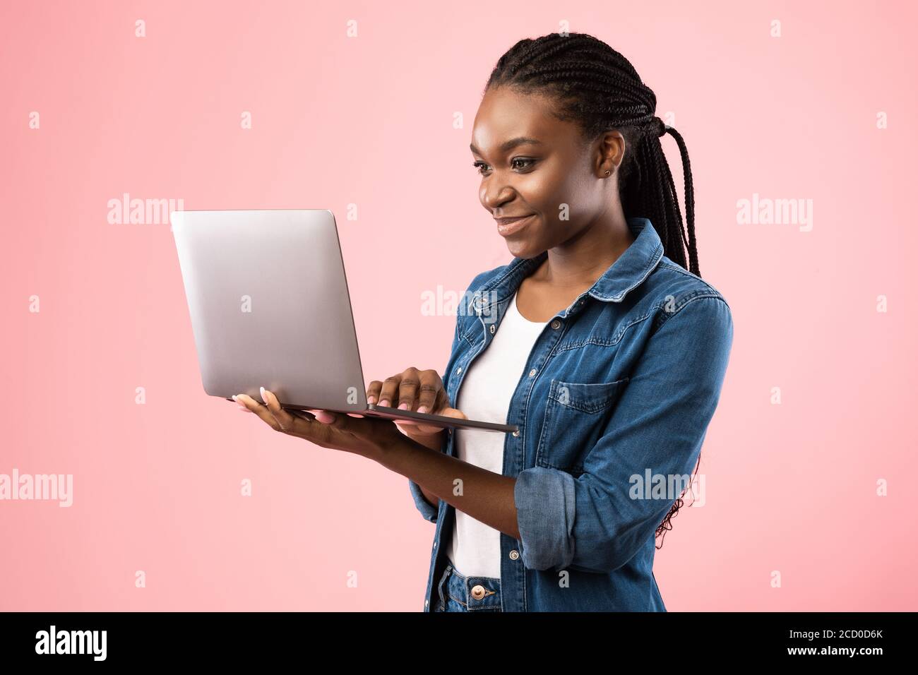 Fille étudiante noire tenant ordinateur portable debout sur fond rose Banque D'Images