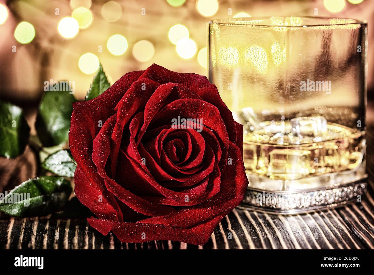 Verre de whisky écossais et de glace , rose rouge dans l'arrière-plan flou coloré de vacances sur table en bois Banque D'Images