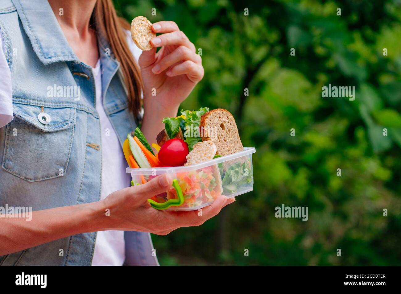 Concept de nourriture saine : jeune fille de hipster manger à partir de la boîte à lunch remplie de sandwich, pains croustillants, fruits et légumes à l'extérieur. Mise au point sélective sur lu Banque D'Images