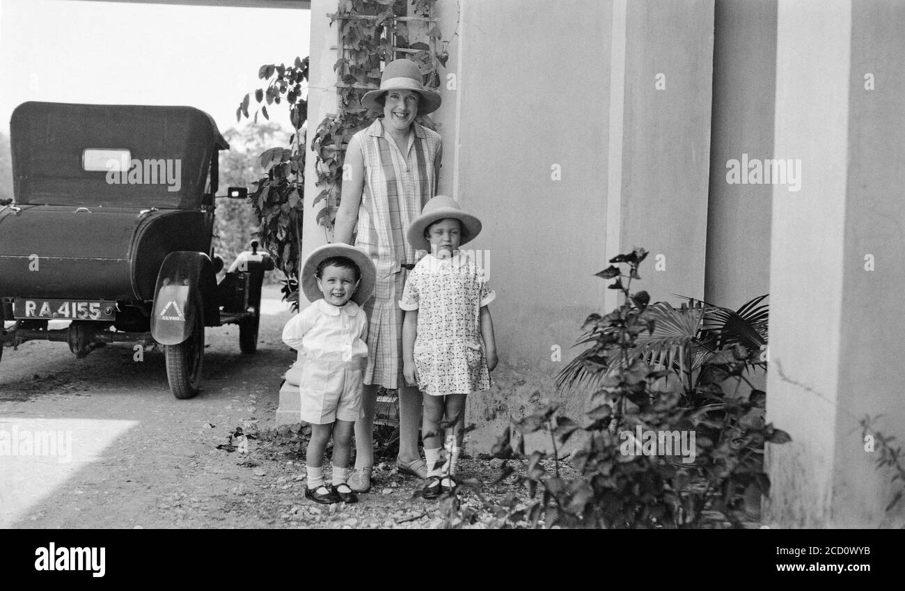 Photographie en noir et blanc des années 1920 montrant une femme avec deux jeunes enfants posant dans une maison. Il y a une voiture britannique Clyno parking, numéro d'immatriculation RA 4155. Banque D'Images