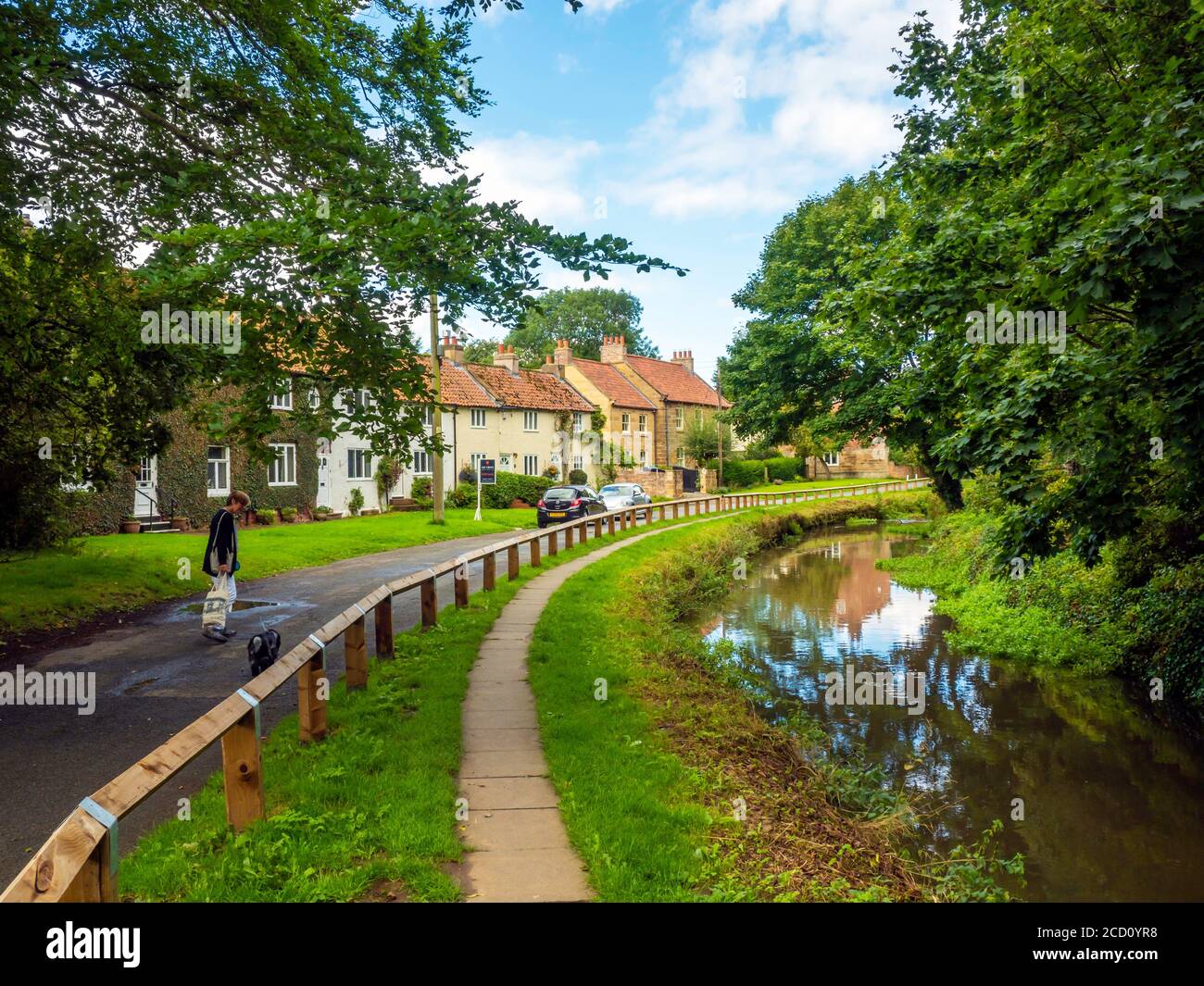 Une femme avec un chien et un chariot de shopping appréciant Une promenade sur un sentier au bord de la rivière Leven in Centre-ville de Stokesley par une belle journée d'été Banque D'Images