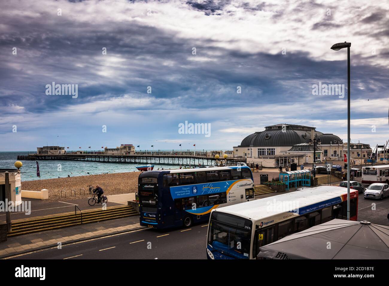 Avec des vents forts qui soufflent les drapeaux sur la jetée, un cycliste solitaire passe devant les bus vides pour battre la tempête de pluie qui suit souvent le vent. Banque D'Images