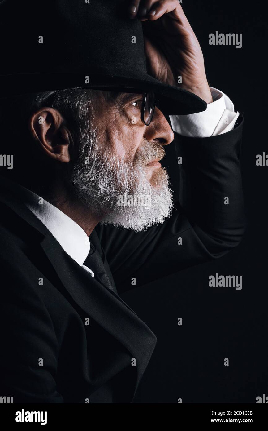 Homme barbu d'âge ancien, à l'image d'un agent secret anglais portant un  costume noir avec chapeau sur les yeux posé sur un fond sombre Photo Stock  - Alamy