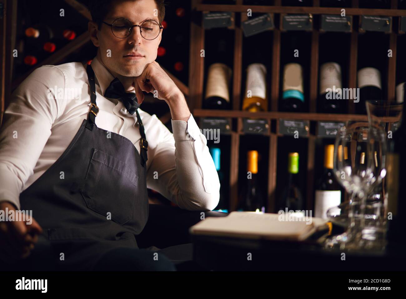 Portrait d'un sommelier mâle regardant l'appareil photo tout en étant assis à la taverne de l'hôtel, qui offre une grande sélection de vins. Industrie du vin. Professions. Banque D'Images