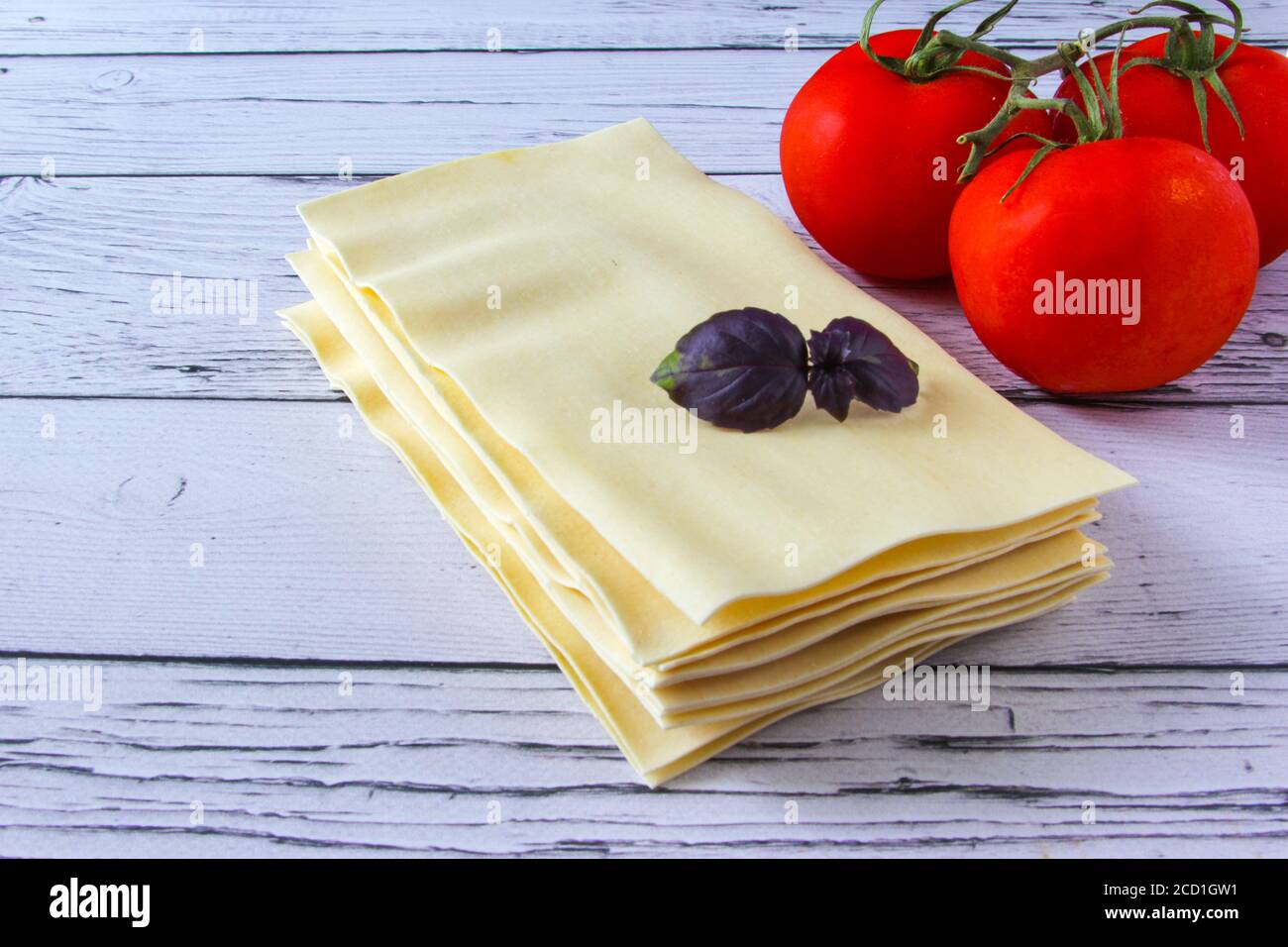 Feuilles de lasagne pâtes avec feuille de tomate et de basilic sur fond de bois. Ingrédients pour une recette italienne. Copier l'espace. Banque D'Images