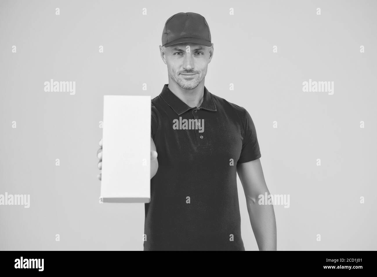 Votre colis entre nos mains sûres. Emballage garçon dans fond jaune uniforme rouge. Boîte de maintien du liveur. Colis de montant de colis. Livré à votre destination, espace de copie. Banque D'Images