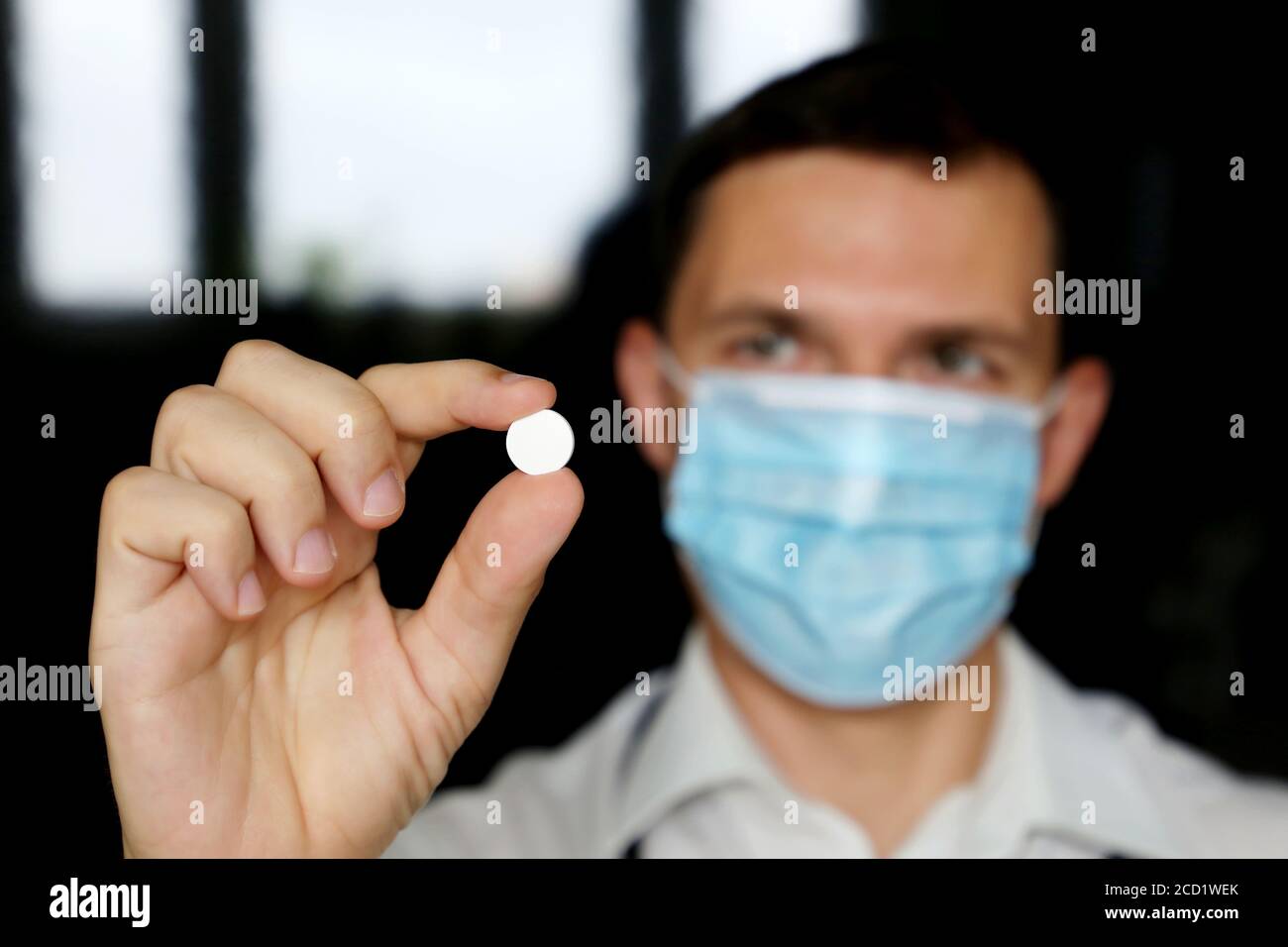 Médecin dans le masque médical tenant la pilule blanche, main masculine avec le médicament de près. Concept de pharmacien, médicaments, antibiotique ou vitamine Banque D'Images