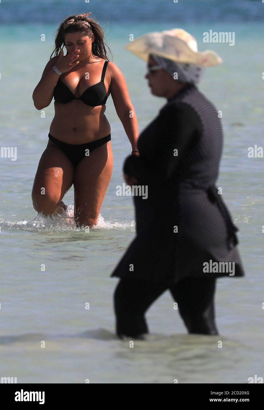 Un touriste portant un bikini marche près d'une femme portant un « burkini  », un maillot de bain intégral conçu pour les femmes musulmanes, pendant des  vacances d'été sur la plage d'Orange
