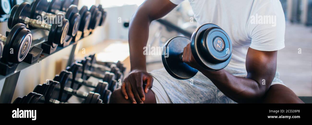 Young African American man et levage un haltère près de la grille à une salle de sport. La formation de poids mâle personne faisant un biceps curl dans le centre de remise en forme Banque D'Images