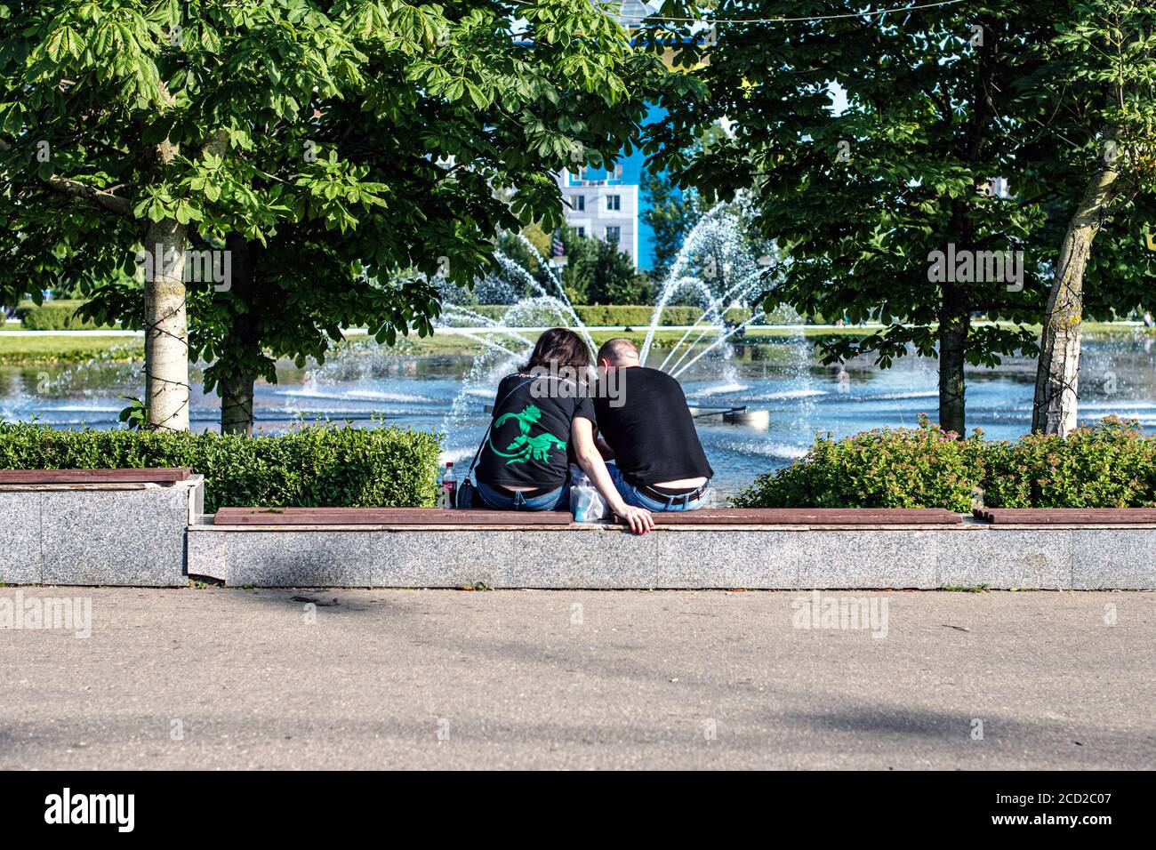 joyeux jeune couple amoureux assis devant un fontaine sur la pelouse du parc Banque D'Images