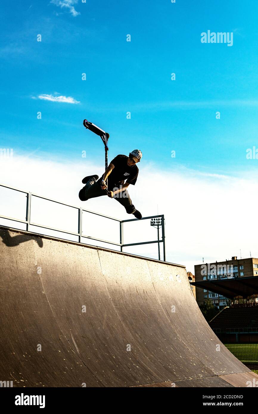 L'adolescent sur le scooter dans un saut contre le fond du ciel. Rétroéclairage. Banque D'Images