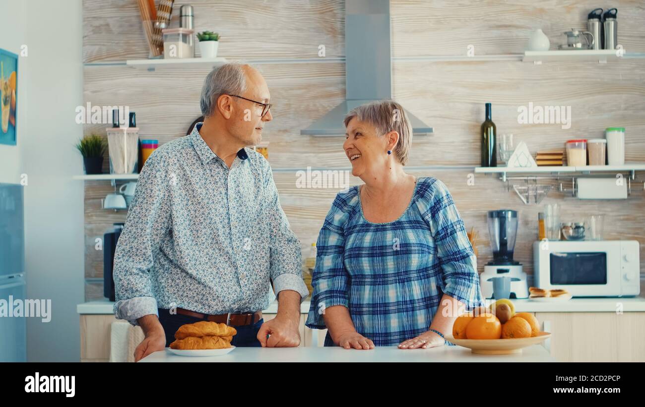 Bât au ralenti d'un couple senior dans la cuisine souriant les uns aux autres et regardant la caméra. Femme et mari joyeux. Banque D'Images
