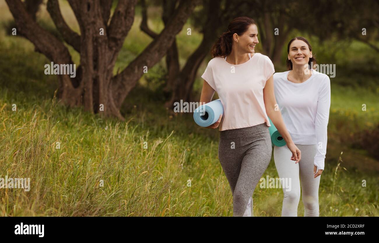 Les femmes de fitness heureux appréciant leur promenade dans un parc tenant des tapis de yoga. Les femmes qui vont faire de l'exercice à l'extérieur le matin. Banque D'Images