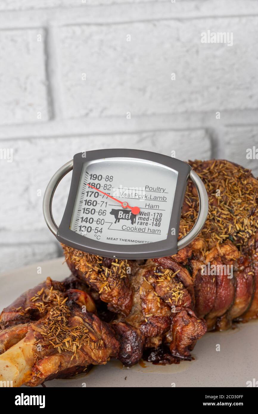 Thermomètre à viande vérifiant la température dans un rôti d'agneau. Avec une garniture de romarin sur une assiette. Banque D'Images