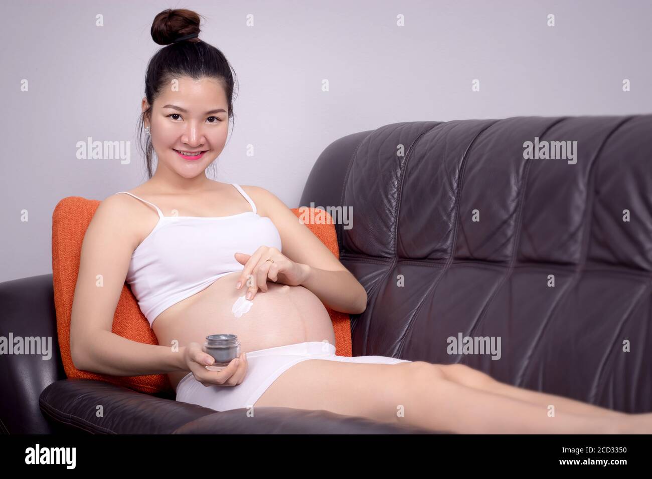 Concept de soins du corps enceinte : la jeune femme enceinte applique de la crème sur son ventre Banque D'Images