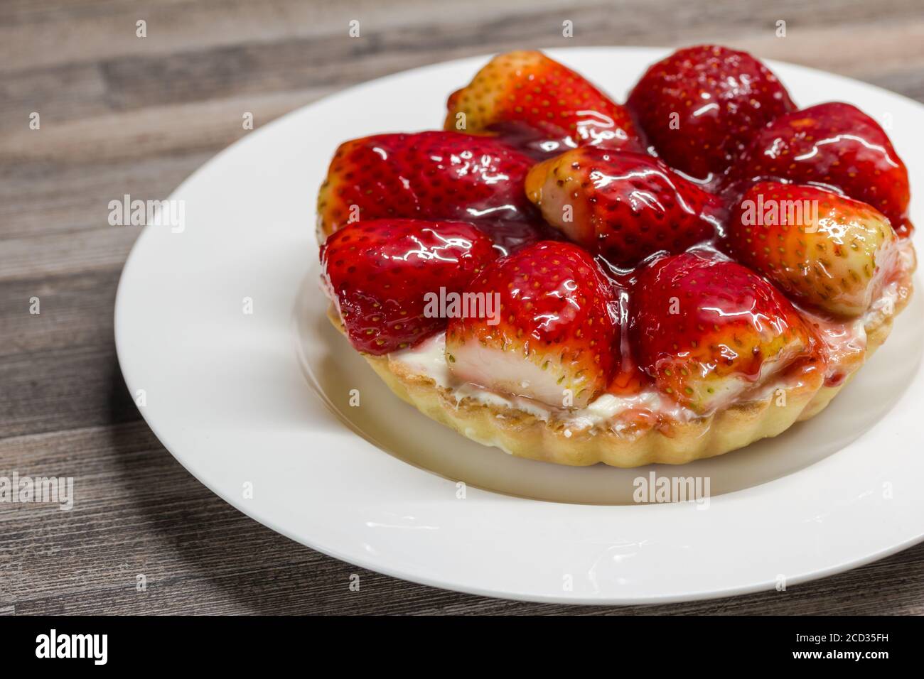 Petite tarte aux fraises avec garniture au cheesecake et base de pâte à croûte courte sur plaque en porcelaine blanche Banque D'Images