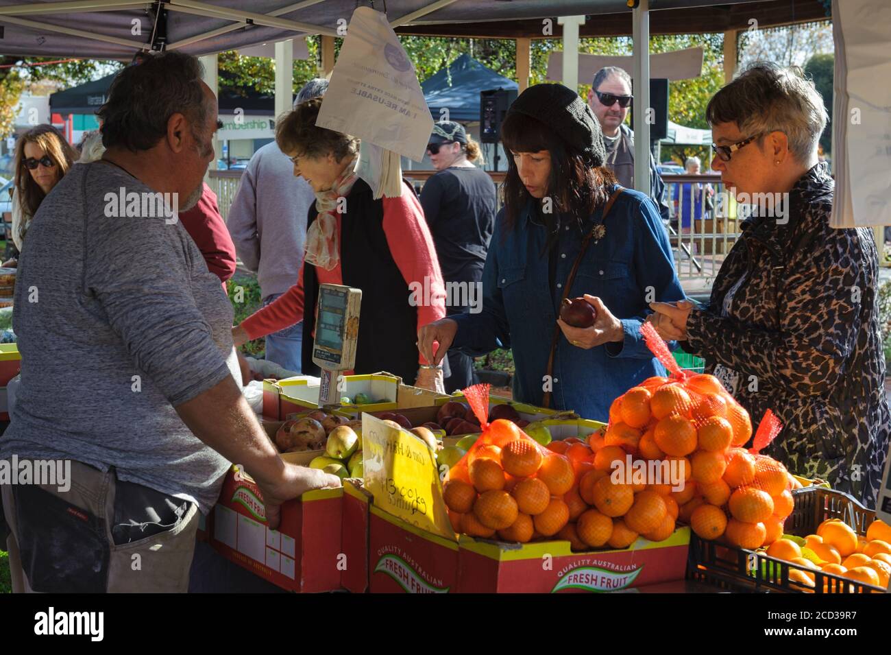 Un vendeur de sexe masculin attend patiemment deux touristes féminins pour choisir une sélection de fruits au marché agricole Victor Harbor en Australie méridionale. Banque D'Images