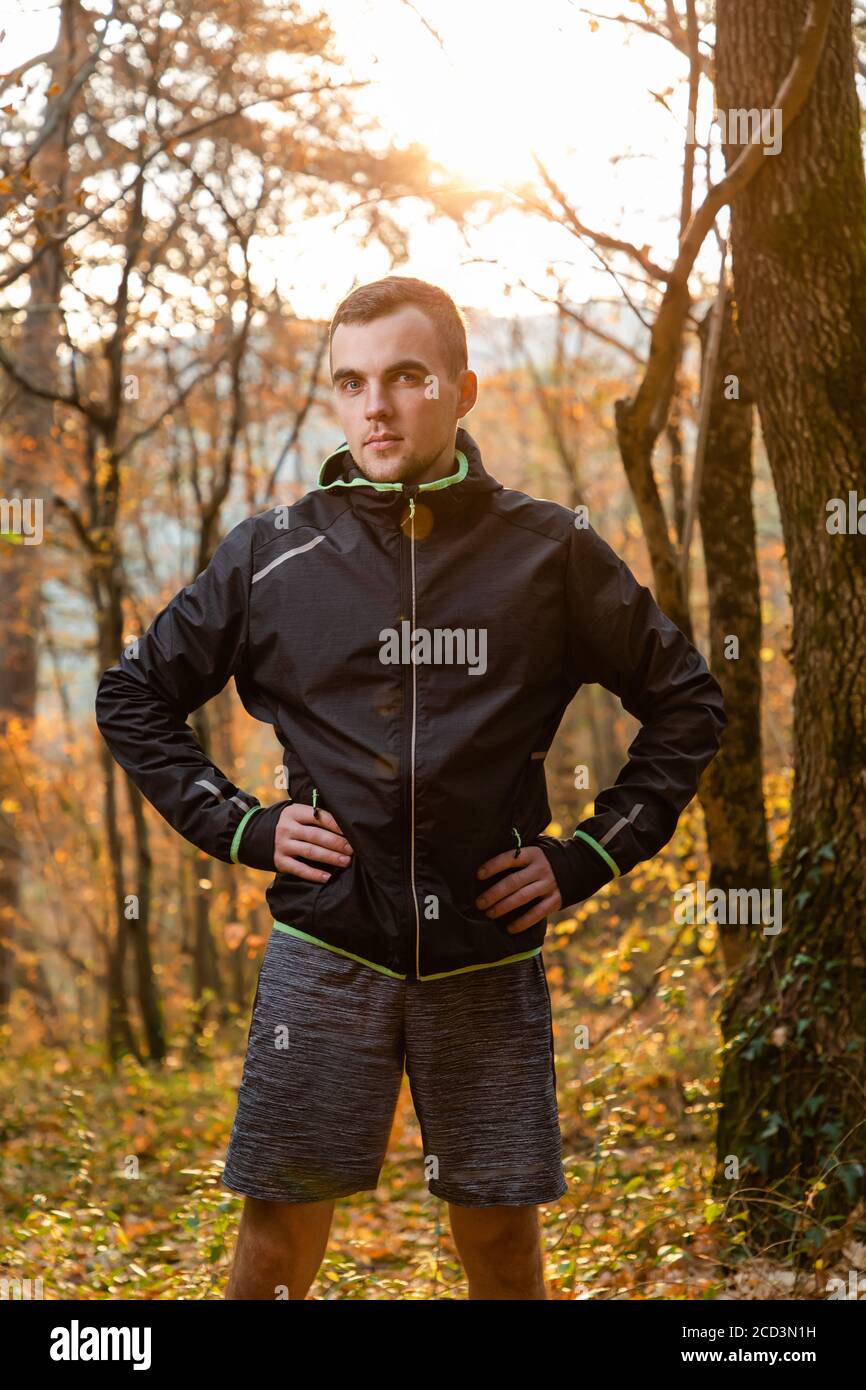 Concept de sport et de mode de vie actif. Un jeune homme dans une combinaison noire, posant dans la forêt d'automne. Verticale. Banque D'Images