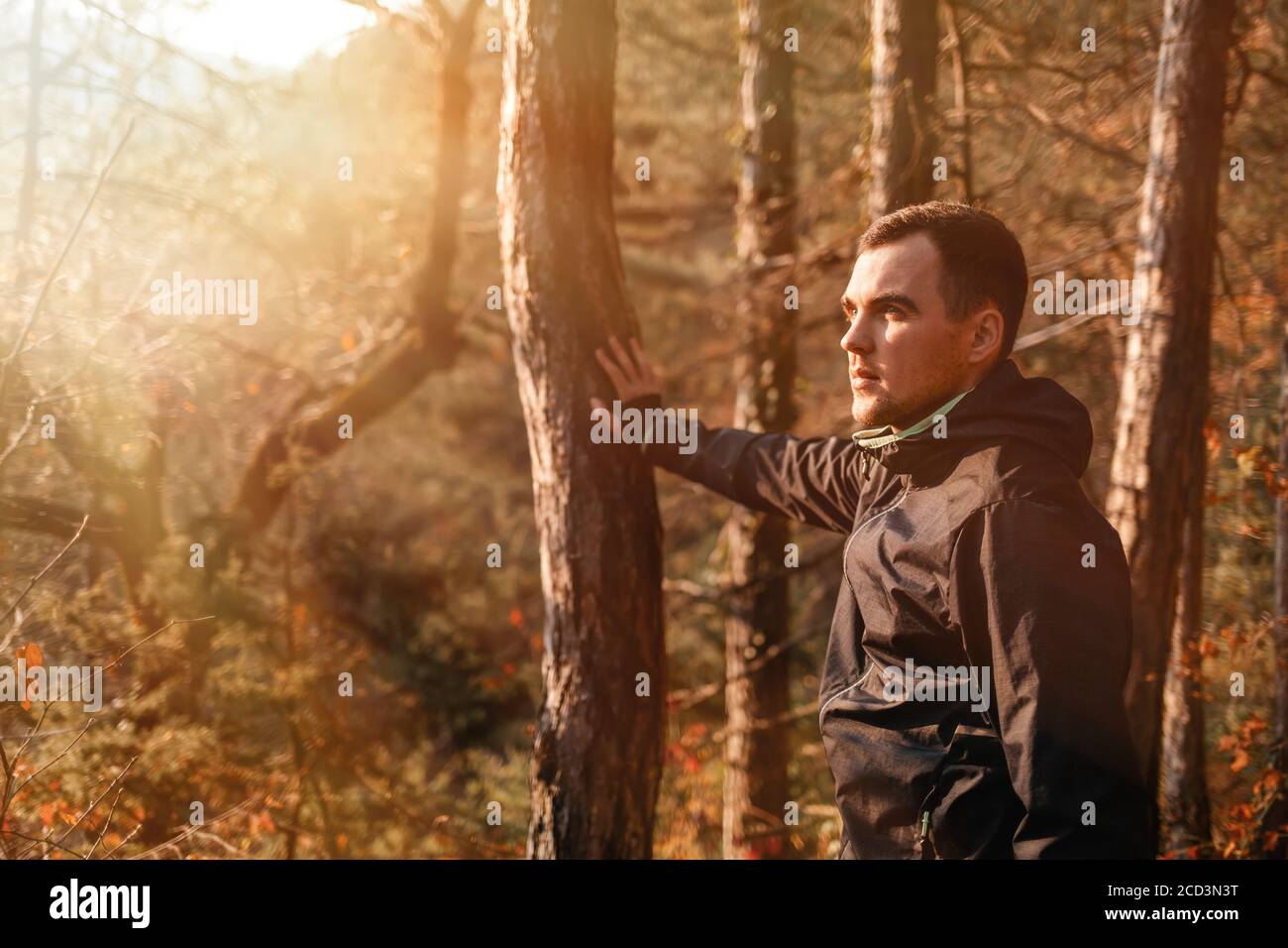 Concept de sport et de mode de vie actif. Un jeune homme dans un survêtement noir, posant près d'un tronc d'arbre. Automne. Lumière du soleil. Copier l'espace Banque D'Images