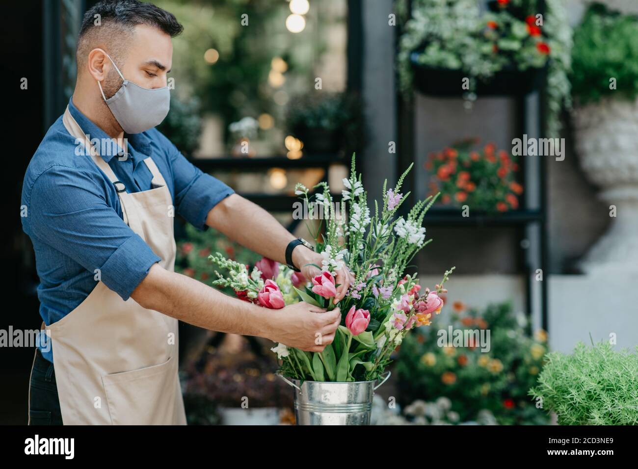Studio à motif fleuri. Un gars occupé dans un tablier et un bouquet de masque dans le magasin Banque D'Images