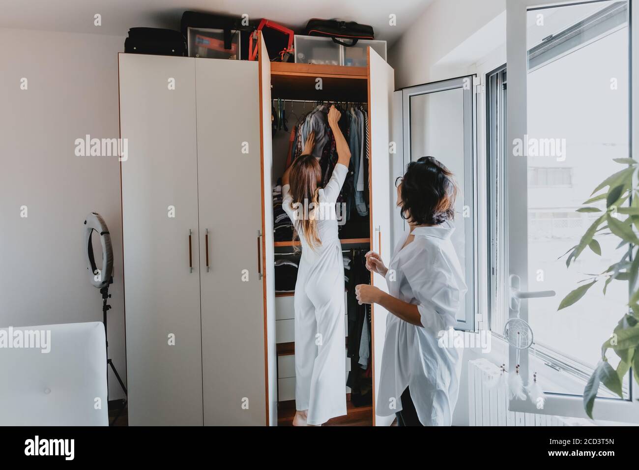 Deux femmes aux cheveux bruns debout dans un appartement, pendent des vêtements dans une armoire. Banque D'Images