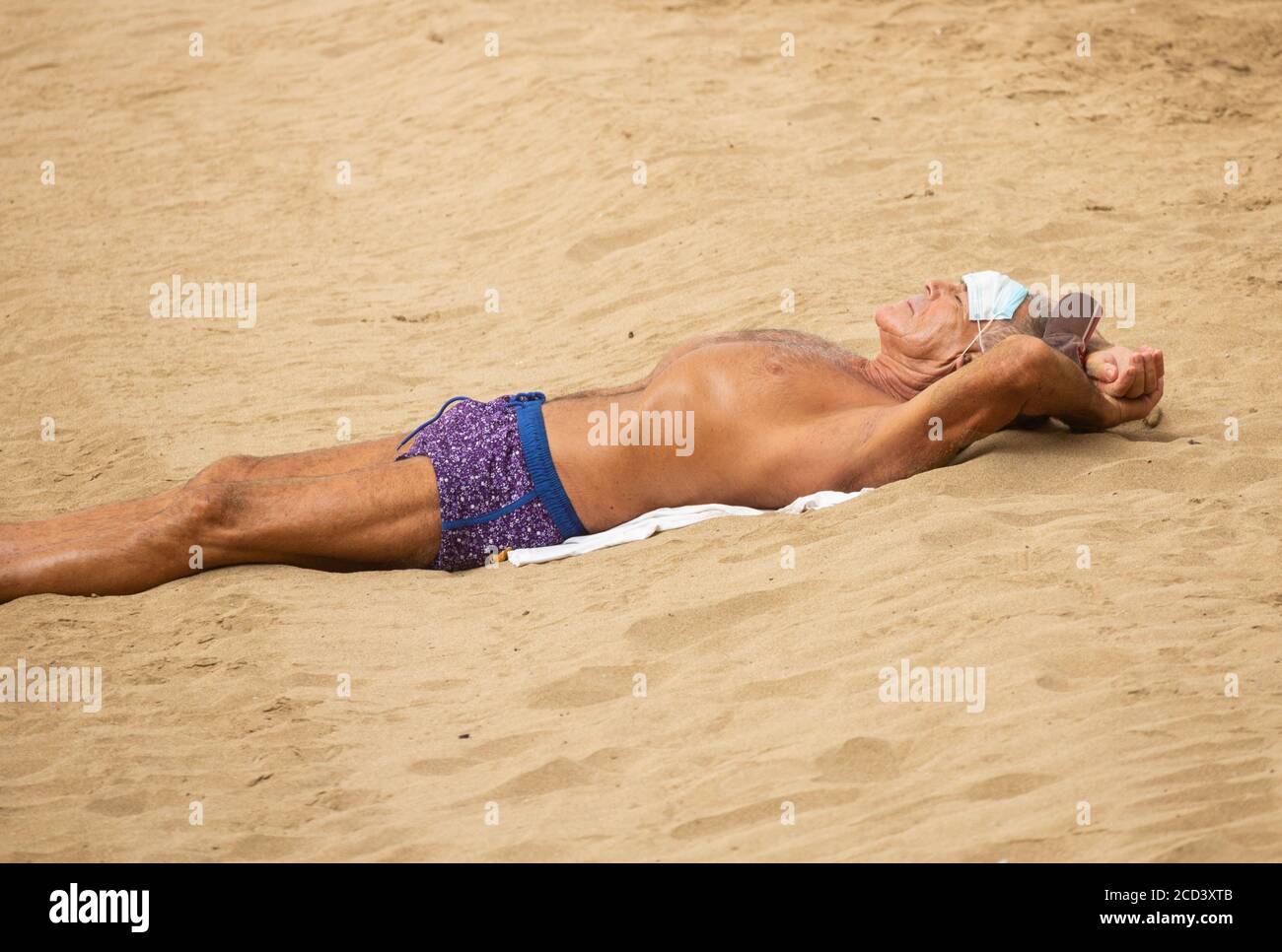 Las Palmas, Grande Canarie, Îles Canaries, Espagne. 26 août 2020. Un soleil porte son masque facial sur le front hise le jour calme sur la plage de la ville à Las Palmas sur Gran Canaria. Avec la montée de 19 cas de Covid sur la Grande Canarie, le gouvernement local a interdit le jogging sur la promenade de la plage pendant la journée et interdit les bains de soleil sur la plage à marée haute pour éviter la foule. Plus de nouveaux cas de coronavirus ont été enregistrés au cours du mois d'août sur la Grande Canarie qu'au cours des mois de mars à août combinés. Plus de 100 des nouveaux cas ont été retracés à une discothèque dans la capitale Las Palmas Banque D'Images