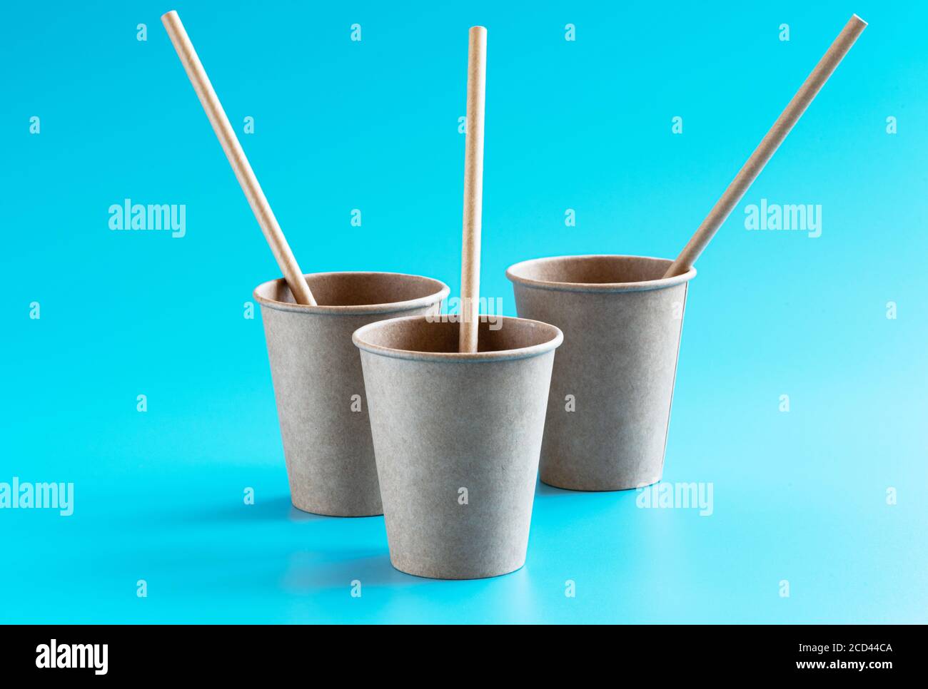 Trois gobelets en papier marron à usage unique et respectueux de l'environnement avec pailles en papier sur fond bleu. Concept sans plastique et sans déchets Banque D'Images
