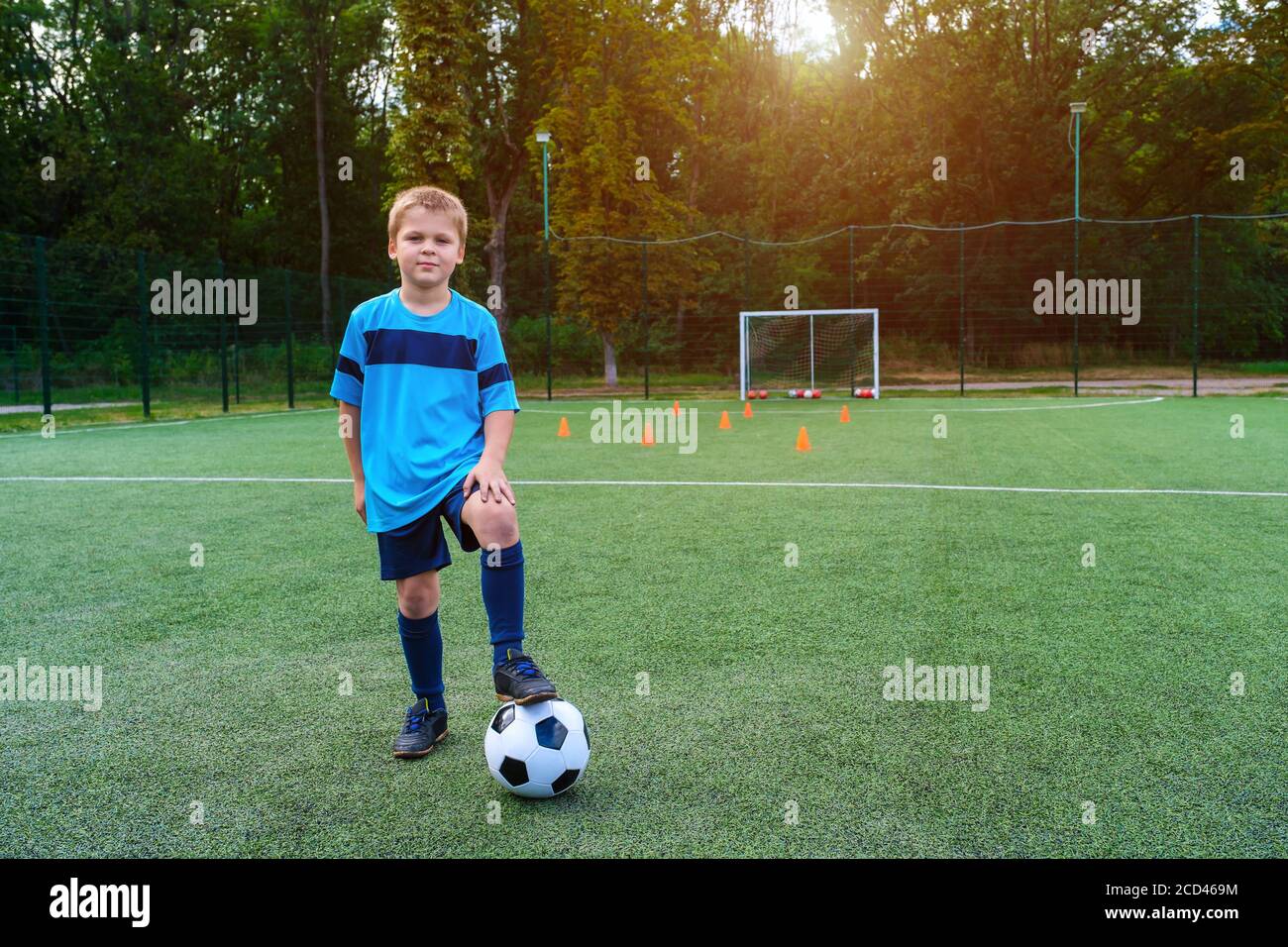 Portrait complet d'un enfant en vêtements de sport posé avec un ballon de football à l'extérieur Banque D'Images