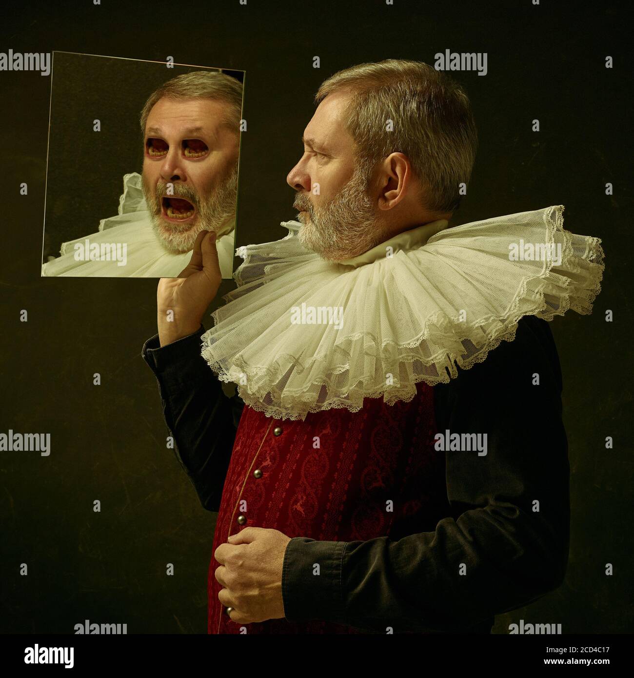 Homme médiéval âgé vêt de vêtements vintage rouges comme un roi ou un prince posant sur un arrière-plan sombre de studio. Concept de comparaison des époques, de la modernité et de la renaissance. Surréaliste regarder avec la bouche au lieu des yeux. Banque D'Images Homme médiéval âgé vêt de vêtements vintage rouges comme un roi ou un prince posant sur un arrière-plan sombre de studio. Concept de comparaison des époques, de la modernité et de la renaissance. Surréaliste regarder avec la bouche au lieu des yeux. Banque D'Images