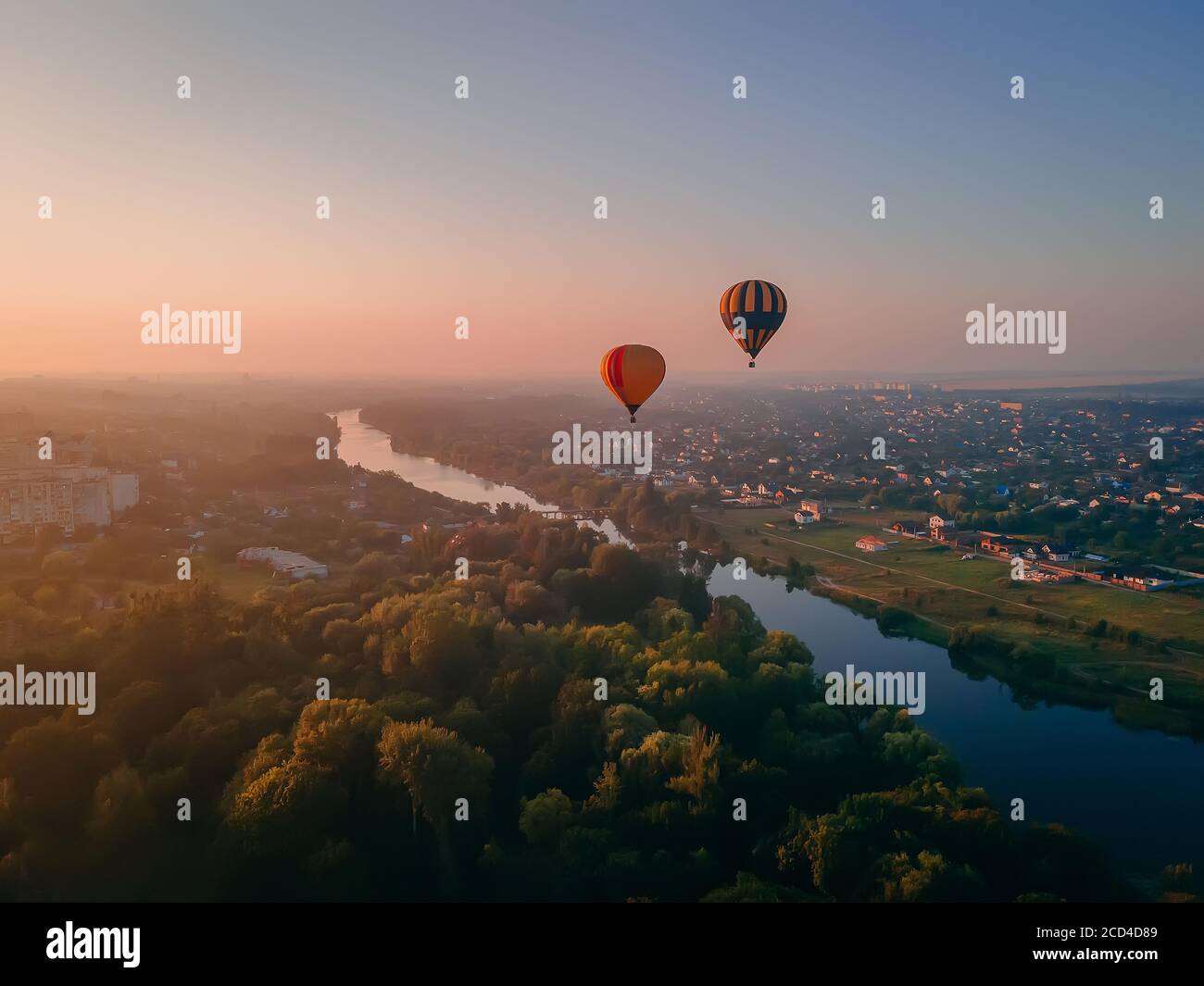 Deux ballons d'air colorés volant au-dessus du parc vert et de la rivière dans la petite ville européenne au lever du soleil d'été, région de Kiev, Ukraine Banque D'Images