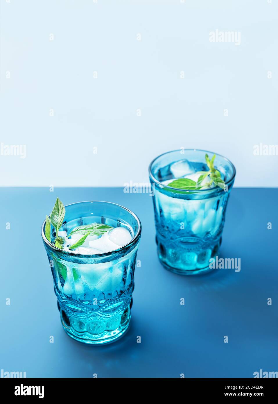 Deux magnifiques verres bleus vintage avec boisson froide et glaçons, avec feuilles de menthe verte fraîche sur fond bleu profond et bleu clair. Toile de fond pour votre conception. Banque D'Images