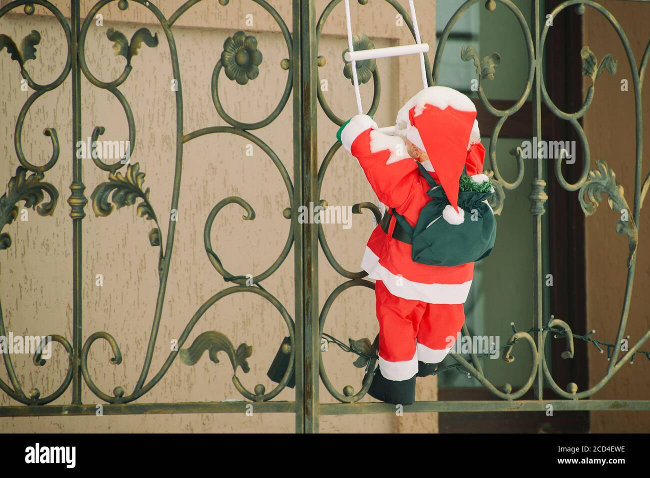 Le Père Noël recouvert de neige monte sur le balcon de l'échelle à corde. Installation de Noël Banque D'Images