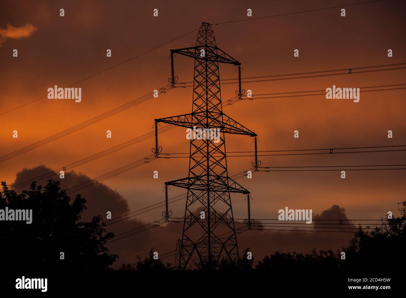 Pylônes d'électricité alimentant la région de l'ouest du pays de Galles lors d'une soirée où les couchers de soleil une orange profonde parmi les nuages. Banque D'Images