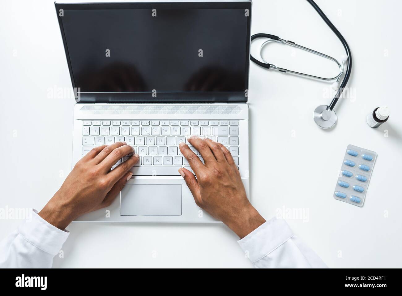 vue de dessus des mains d'une femme médecin afro utilisation d'un ordinateur portable sur le dessus d'un bureau blanc avec pilules et stéthoscope Banque D'Images