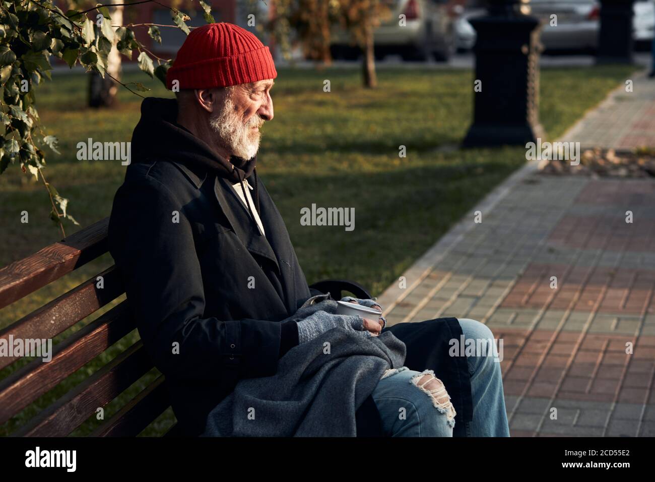 Homme mature sans abri assis dans des vêtements de rue sur le banc, sans nourriture et sans argent. Un homme qui courait a baissé la tête. Vue latérale sur le perso sans-abri Banque D'Images