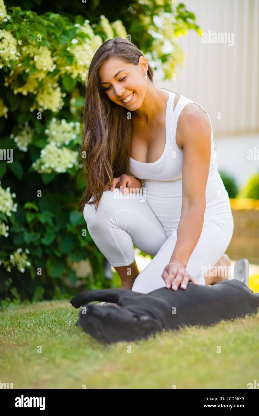 Smiling femme enceinte avec un gros ventre tape son chien dans le jardin Banque D'Images