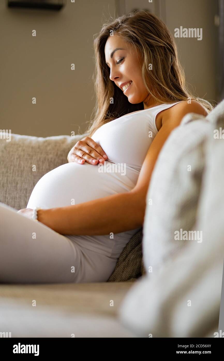 Smiling pregnant woman sitting in canapé en regardant son ventre Banque D'Images