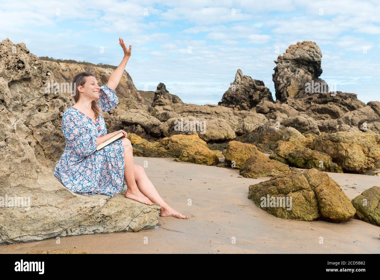 Femme pieds nus assise sur un rocher qui agite sur la plage Banque D'Images