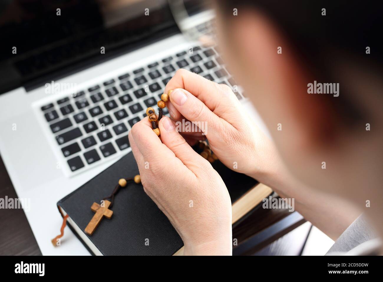 Prière Rosaire en ligne, messe sainte conduite en ligne. Foi et prière. Une femme prie le rosaire. Une femme prie sur un rosaire devant un ordinateur. Banque D'Images