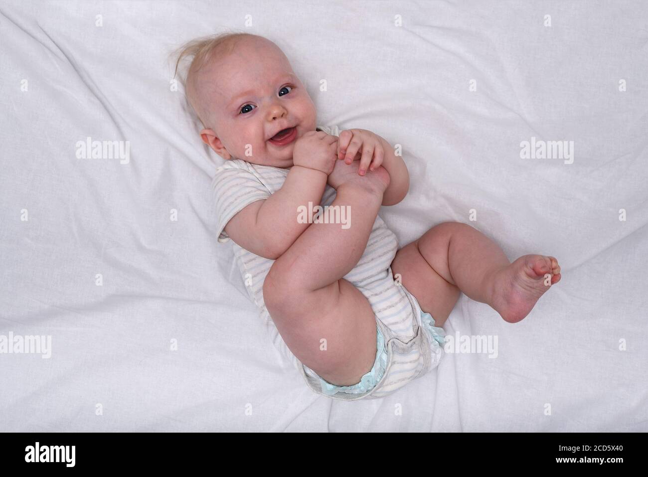 Joyeux mignon bébé fille de 3 mois avec les cheveux blonds courts allongé sur le tissu blanc couches. Couches pour nouveau-nés. Banque D'Images Joyeux mignon bébé fille de 3 mois avec les cheveux blonds courts allongé sur le tissu blanc couches. Couches pour nouveau-nés. Banque D'Images