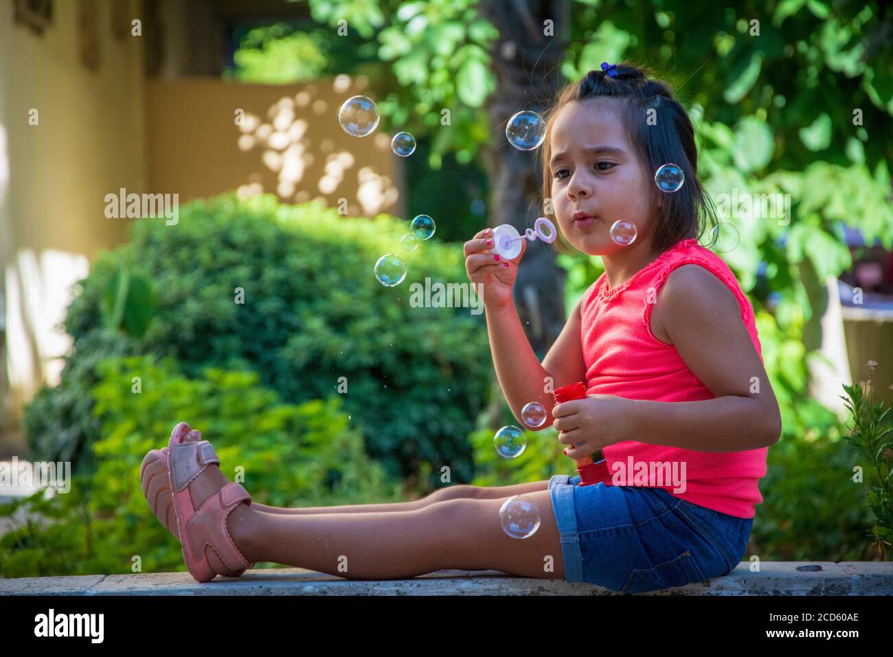 Une petite fille vêtue de vêtements décontractés souffle des bulles le jardin Banque D'Images